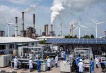 NASENI Quietly Rewriting Nigeria’s Industrial Story Nigerian engineers in lab coats work with advanced machinery in a modern industrial facility, surrounded by solar panels, wind turbines, and rising smokestacks under a bright sky.
