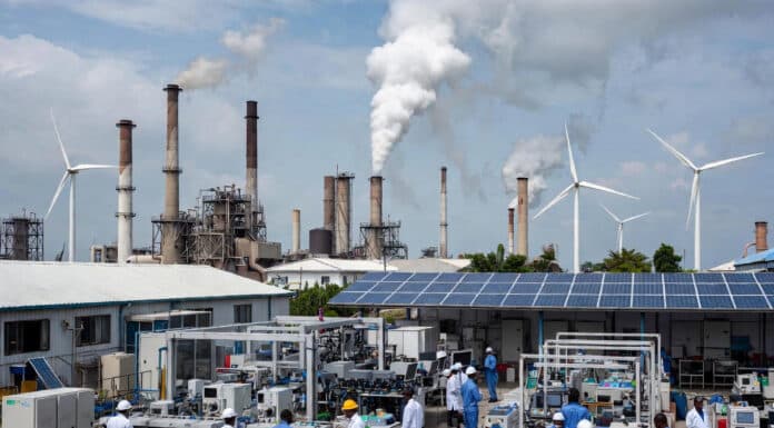 Nigerian engineers in lab coats work with advanced machinery in a modern industrial facility, surrounded by solar panels, wind turbines, and rising smokestacks under a bright sky.
