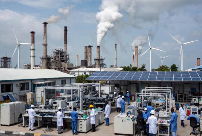 Nigerian engineers in lab coats work with advanced machinery in a modern industrial facility, surrounded by solar panels, wind turbines, and rising smokestacks under a bright sky.