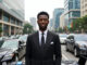 Who Is the Youngest Billionaire in Nigeria? Alt Text: Confident young Nigerian billionaire in a sharp suit stands on a Lagos business street surrounded by luxury cars and skyscrapers.