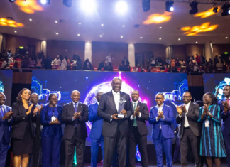 Enoch Ogunnowo smiling on stage holding the Nigeria Technology Awards 2023 trophy, with bright stage lights and the NiTA logo in the background.