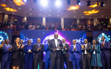 Enoch Ogunnowo smiling on stage holding the Nigeria Technology Awards 2023 trophy, with bright stage lights and the NiTA logo in the background.