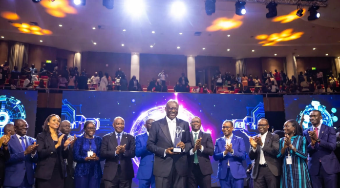 Enoch Ogunnowo Honoured at Nigeria Technology Awards 2023 Enoch Ogunnowo smiling on stage holding the Nigeria Technology Awards 2023 trophy, with bright stage lights and the NiTA logo in the background.