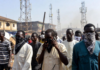 Bandits Bounce Calls Off Multiple Towers – Minister Masked individuals using mobile phones in front of multiple telecom towers in a dusty Nigerian rural area, illustrating bandits evading security forces by routing calls through different base stations.