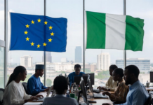EU Commits €45 Million to Boost Nigeria’s Digital Economy Nigerian and European officials in a modern conference room with EU and Nigerian flags, collaborating on laptops against a Lagos city skyline, symbolising partnership in digital innovation.