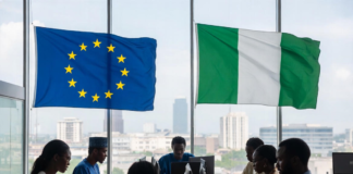 EU Commits €45 Million to Boost Nigeria’s Digital Economy Nigerian and European officials in a modern conference room with EU and Nigerian flags, collaborating on laptops against a Lagos city skyline, symbolising partnership in digital innovation.