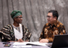 Nigeria and Indonesia Enhance Livestock Technology Exchange Nigerian official in traditional attire and Indonesian livestock expert reviewing digital tablet together, with background overlays of modern cattle farms, AI monitoring systems and dairy processing plants.