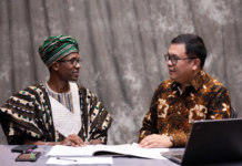 Nigerian official in traditional attire and Indonesian livestock expert reviewing digital tablet together, with background overlays of modern cattle farms, AI monitoring systems and dairy processing plants.