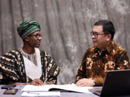 Nigerian official in traditional attire and Indonesian livestock expert reviewing digital tablet together, with background overlays of modern cattle farms, AI monitoring systems and dairy processing plants.