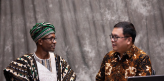 Nigerian official in traditional attire and Indonesian livestock expert reviewing digital tablet together, with background overlays of modern cattle farms, AI monitoring systems and dairy processing plants.