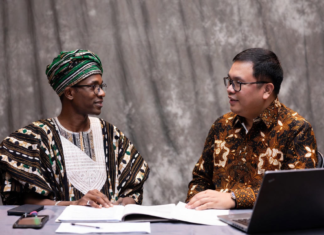 Nigeria and Indonesia Enhance Livestock Technology Exchange Nigerian official in traditional attire and Indonesian livestock expert reviewing digital tablet together, with background overlays of modern cattle farms, AI monitoring systems and dairy processing plants.