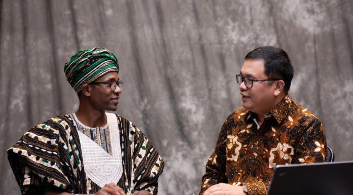 Nigerian official in traditional attire and Indonesian livestock expert reviewing digital tablet together, with background overlays of modern cattle farms, AI monitoring systems and dairy processing plants.