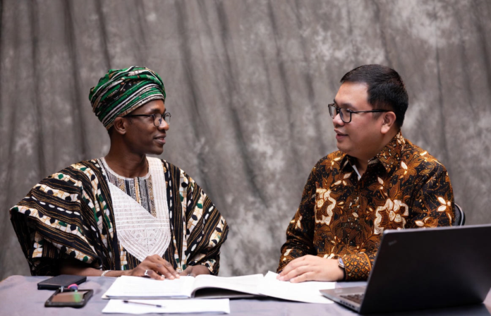 Nigerian official in traditional attire and Indonesian livestock expert reviewing digital tablet together, with background overlays of modern cattle farms, AI monitoring systems and dairy processing plants.